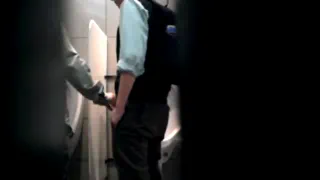 Мужчина в общественной туалетах неуклюже справляющийся с делами у урны со своей рюкзаком
