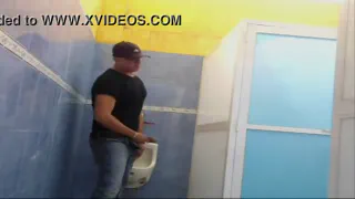 Мускулистый мужчина мочится на унитаз в ванной